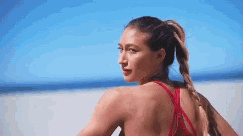 a woman in a red bikini top is standing on a beach looking over her shoulder .