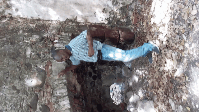 a man in a blue and white striped shirt is standing in a rocky area
