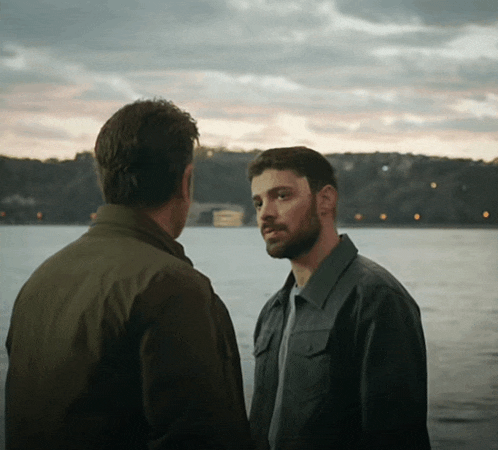 two men are standing in front of a body of water