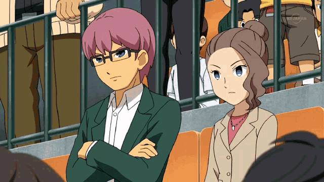 a man and a woman are sitting in a stadium with their arms crossed in front of a tv screen