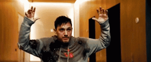 a man in a hoodie is standing in a hallway with his arms in the air .