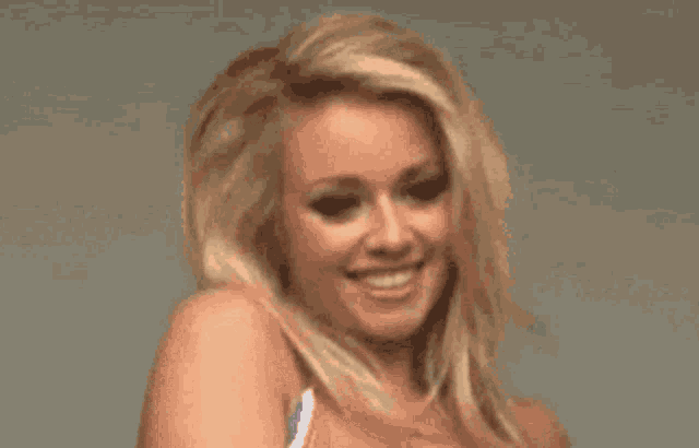 a blonde woman is smiling and looking at the camera while wearing a bikini top .