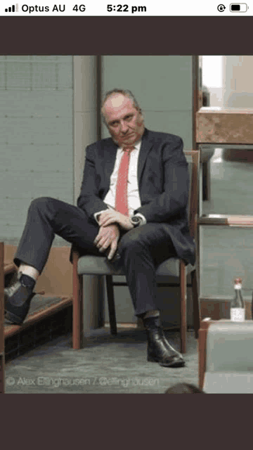 a man in a suit and tie is sitting in a chair with his legs crossed .