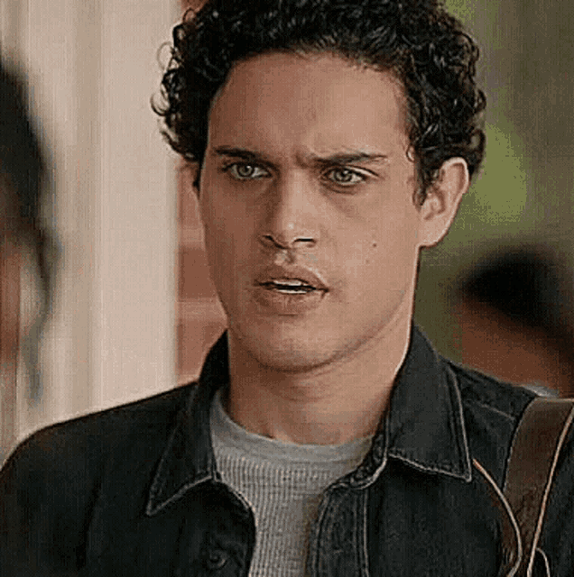 a man with curly hair is wearing a denim jacket and a gray sweater .