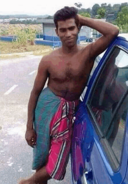 a man without a shirt is leaning against a blue car .
