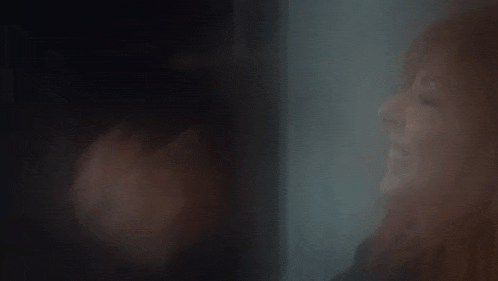 a woman with red hair is looking out of a window in a dark room .