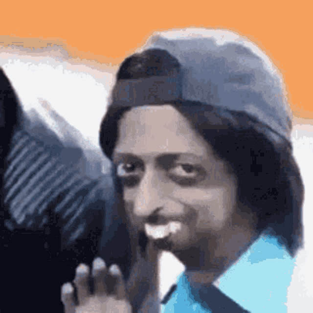 a man wearing a baseball cap and wig is smiling and waving .