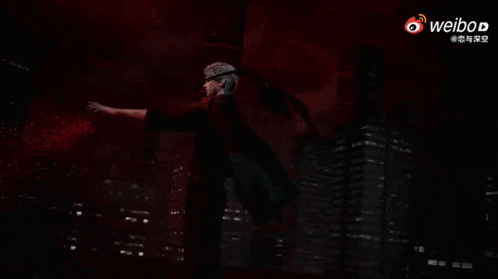 a man in a black shirt is reaching out with his hand in the dark .