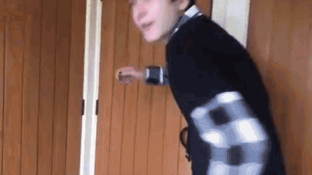 a young boy is standing in front of a wooden door and looking at the camera .