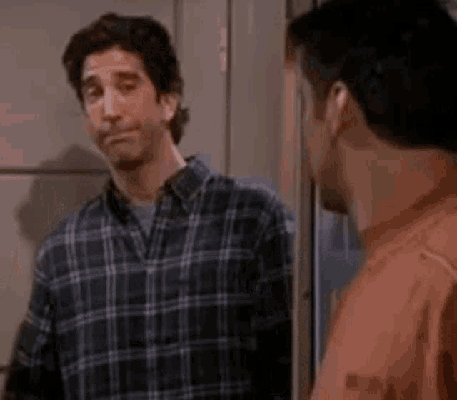a man in a plaid shirt is standing next to another man in an orange shirt in front of a door .