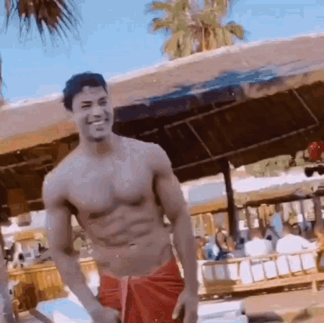 a shirtless man in a red towel is standing on a beach