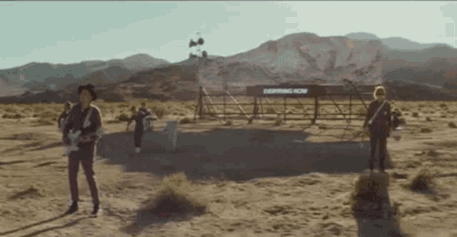 a group of people standing in a desert with a sign that says everything now