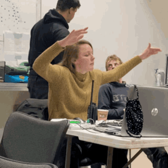 a woman in a yellow sweater is sitting at a table with her arms outstretched in front of a hp laptop