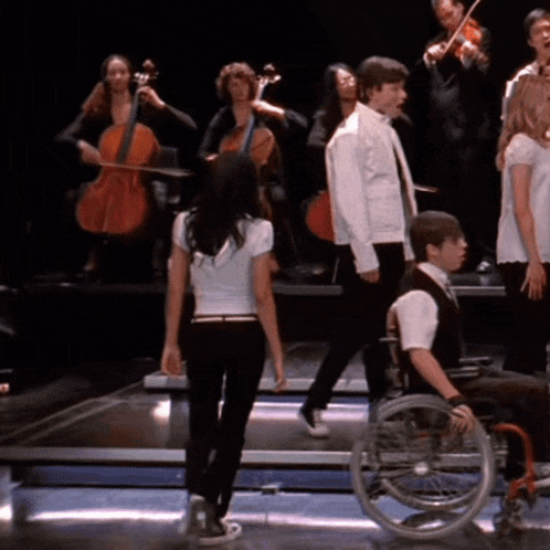 a man in a wheelchair is standing in front of a group of people playing instruments