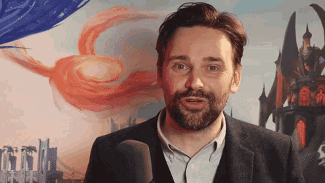 a man with a beard is speaking into a microphone in front of a painting