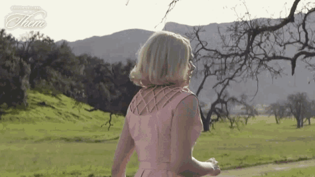 a woman in a pink dress stands in a field with the word them on the bottom left