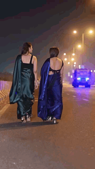 two women walking down a street at night with a police car behind them