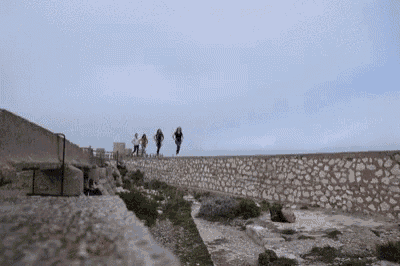 a group of people are walking along a stone wall