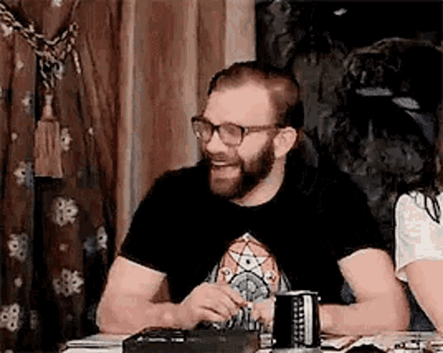 a man with a beard and glasses is sitting at a table with a woman .
