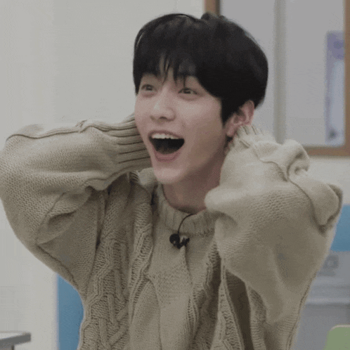 a young man wearing a tan sweater with his mouth wide open