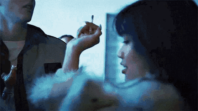 a woman is holding a cigarette in her hand and smoking it while a man looks on .