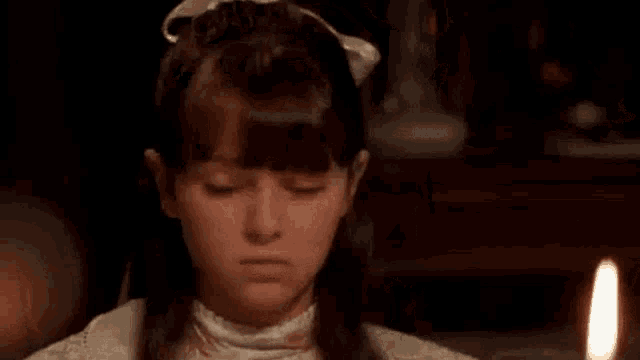 a young girl wearing a white dress and a white bow in her hair is sitting at a table .