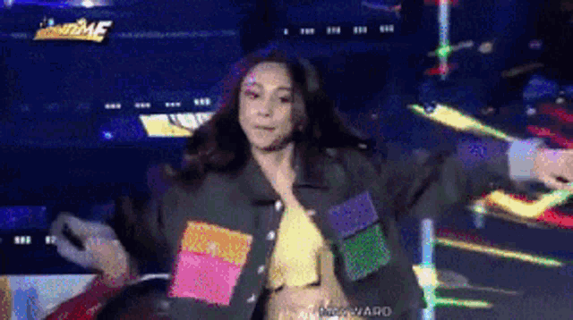 a woman in a black jacket is dancing on a stage in front of a screen that says ' home ' on it