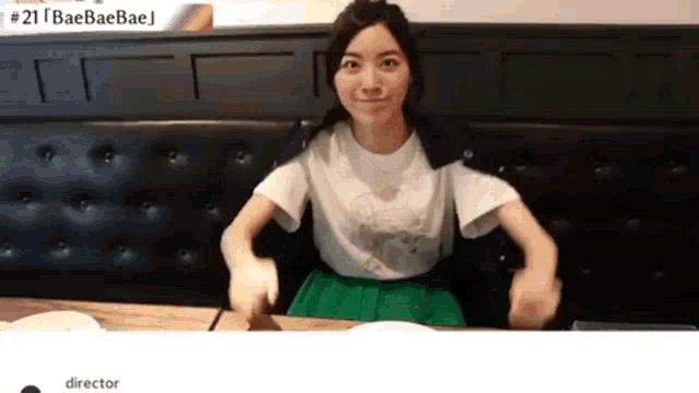 a woman in a white shirt and green skirt is sitting at a table with her arms outstretched .