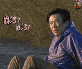 a man in a blue jacket is sitting on the ground laughing with chinese writing behind him .