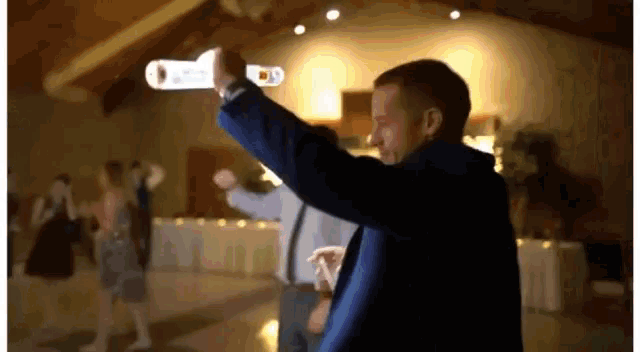 a man in a blue suit is holding a remote control in his hand while dancing at a wedding reception .