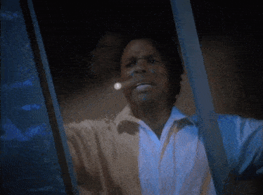 a man in a white shirt is looking out of a window with his mouth open .