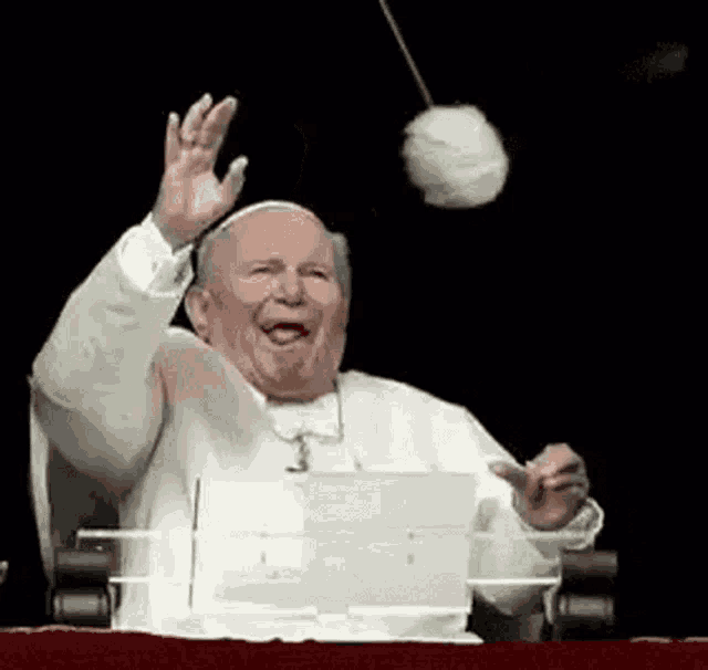 a man in a white robe is sitting on a balcony while a ball is being tossed at him .