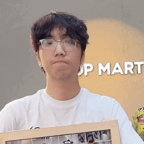 a man wearing glasses and a white shirt is holding a picture frame in front of a sign that says op mart