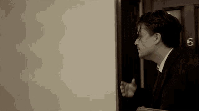 a man in a suit is standing in front of a door that has the number 6 on it