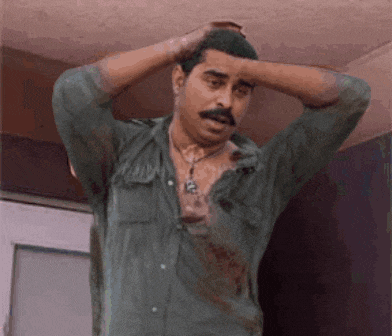 a man with a mustache is holding his head while wearing a green shirt