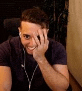 a man is sitting at a desk wearing headphones and smiling while covering his face with his hand .