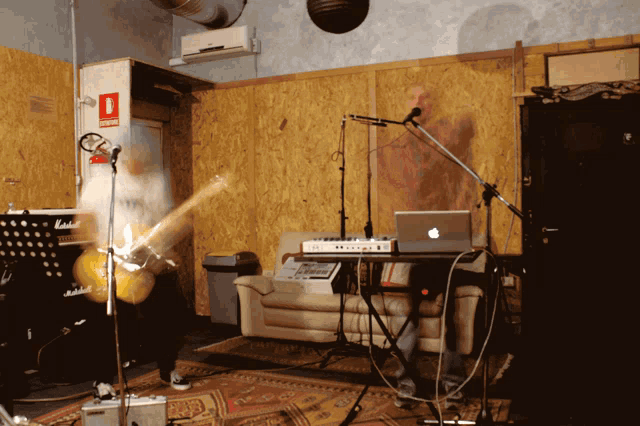 a man is playing a guitar in front of a microphone in a room with a red fire extinguisher on the wall