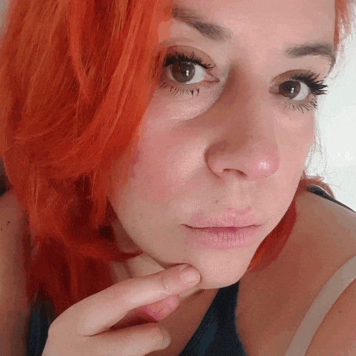 a woman with red hair is touching her face with her hand