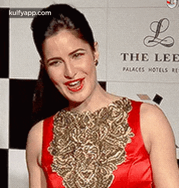 a woman in a red and gold dress is smiling in front of a sign .
