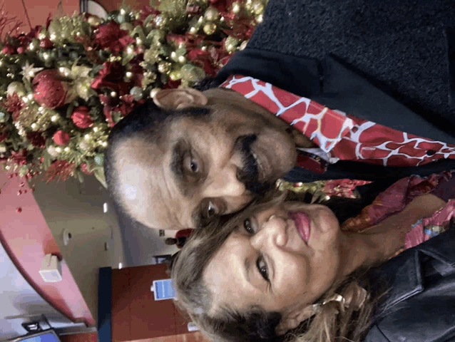 a man and a woman are posing for a photo in front of a christmas tree