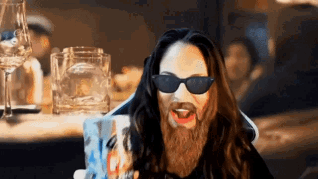 a man with a beard wearing sunglasses holds a mug