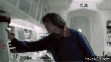 a man is standing in a kitchen reaching for a container .
