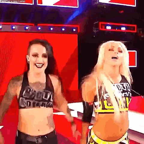 two female wrestlers are standing next to each other on a stage and smiling .