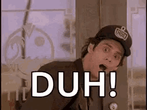 a man wearing a baseball cap is standing in front of a door and says duh .