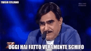 a man with a mustache is sitting in front of a microphone and says oggi hai fatto veramente schifo .