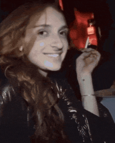a woman is smiling and holding a cigarette in her right hand