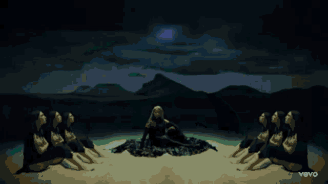 three women are sitting on a sandy beach with the word vevo on the bottom right