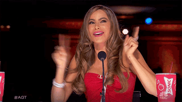 a woman in a red dress giving a thumbs up in front of a microphone