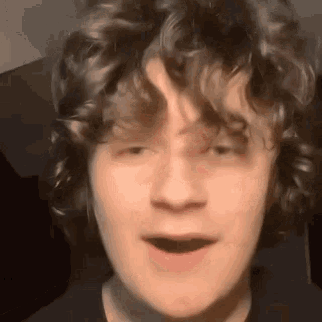 a close up of a young man with curly hair making a funny face with his mouth open .