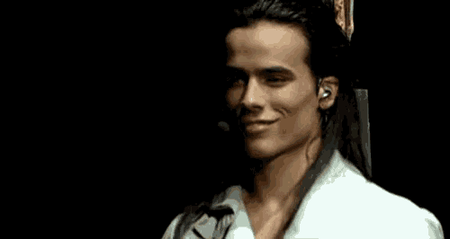 a man with long hair wearing a white shirt and ear buds